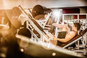 Muscular man pumping legs in machine photo