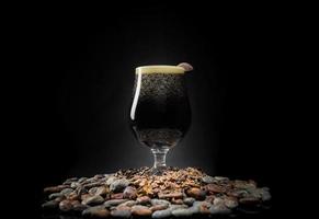 Pinta de cerveza negra oscura sobre un montón de semillas de cacao y frijoles foto