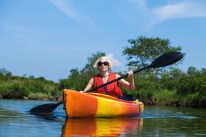Mujer con chaleco de seguridad en kayak solo en un río tranquilo