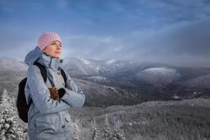 Mujer joven mirando la vista desde la cima de una montaña en invierno