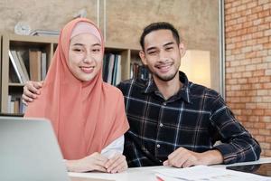 Portrait of entrepreneur business startup persons, young male, and beautiful female owner, two partners who Islamic couple, looking at camera, smiles happily in small e-commerce workplace office. photo