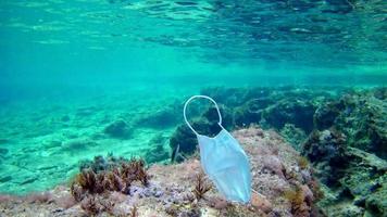 una maschera medica sul fondo del mare e diversi pesci che galleggiano accanto ad essa, come simbolo della protezione contro il covid-19 nelle località balneari. video