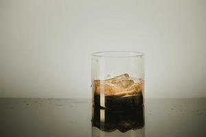 Salpicaduras de vaso de whisky de malta sobre fondo gris foto