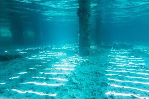 Vista submarina de debajo de un muelle con pilares y luz solar