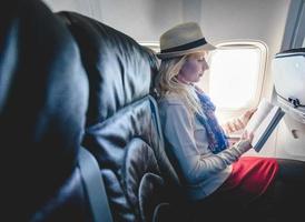 Joven mujer turista caucásica sola leyendo un libro dentro del avión foto