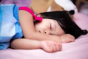 Asian cute little child lying in bed at bedroom. Kid girl sleeping in afternoon. Children sleeping in blue blanket. Daughter aged 3 year old is sleepy. photo