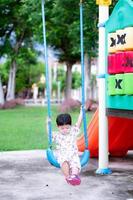 Little boy was sitting on swing. Legs float on the floor. Lightly swing. Toddler kid  aged 2 year old. Handsome child loves blue swings. Children play in playground. photo