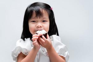 Happy girl bits sweet chocolate cake. She wears white shirt. Sweet smiling. Children's concept with eating sweets.