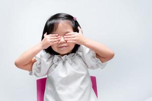 Cute child covered both eyes with her hands. On isolated white background. photo