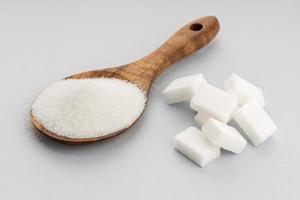 Sugar In Wooden Spoon and sugar cubes on gray background. Close up photo