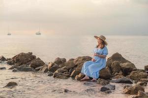 pregnant woman sitting the rocks near the sand beach and the sea. photo