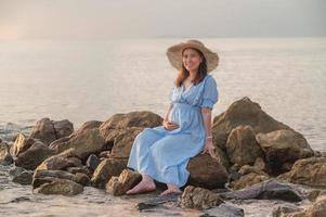 mujer embarazada sentada en las rocas cerca de la playa de arena y el mar. foto