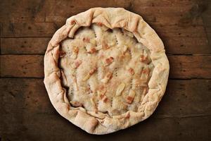 Whole salted pie with bacon on rough wooden table photo