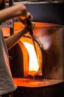 Glassmaker recogiendo pieza de vidrio fundido en el horno con tubo foto