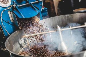 Granos de café tostados humeantes en el cilindro de enfriamiento foto