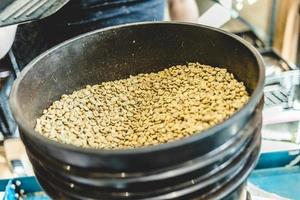 Trabajador de cultivos vertiendo granos de café crudo en tostador foto