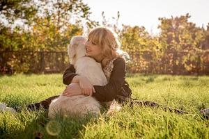 Beautiful caucasian woman hugging her golden labrador retriever dog at a park in the sunset photo