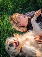 Hermosa mujer caucásica tendido en el césped con su perro labrador retriever dorado en un parque en la puesta de sol foto