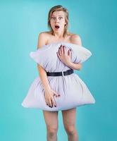 Shocked woman covering herself with a pillow isolated on blue background photo