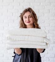 Mujer sonriente sosteniendo un montón de toallas sobre fondo de ladrillos blancos foto