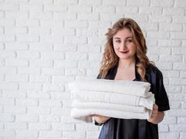 Mujer sonriente sosteniendo un montón de toallas sobre fondo de ladrillos blancos foto