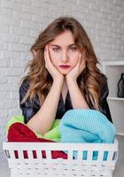 Upset woman doing laundry sitting over a pile of towels on white brick background photo