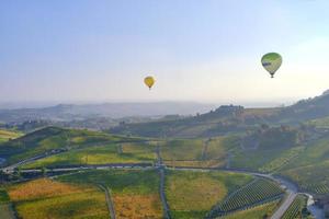 Aerostatic balloons are flying over the hills of Langhe, Piedmont, Northern Italy, covered by vineyards during fall season. UNESCO Site since 2014. photo