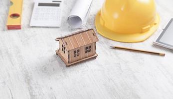 modelo de casa de madera con casco, nivel, documento y lápiz. foto