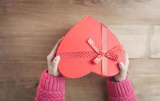 Hands holding a box in the shape of heart on wooden background. photo