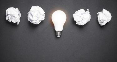 Light bulb and crumpled papers in the black background. Idea photo