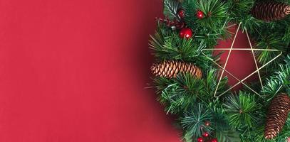 Corona de Navidad de pino verde con estrella y cono de pino, elemento de decoración de cereza sobre fondo de pared roja. Espacio de copia para agregar texto o diseño. foto