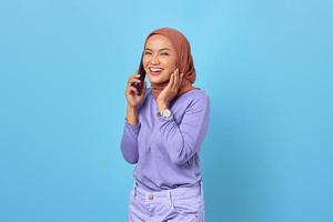 Retrato de mujer asiática joven sonriente hablando por un teléfono móvil sobre fondo azul. foto