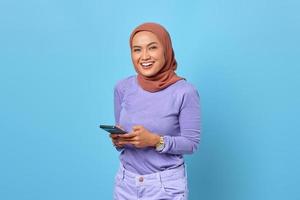 retrato, de, sonriente, joven, mujer asiática, utilizar, un, teléfono móvil, en, fondo azul