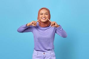 Portrait of attractive young Asian woman pointing at white teeth healthy on blue background