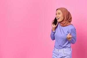 Portrait of smiling young Asian woman talking on a mobile phone on pink background