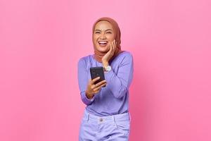 retrato, de, sonriente, joven, mujer asiática, tenencia, teléfono móvil, en, fondo rosa