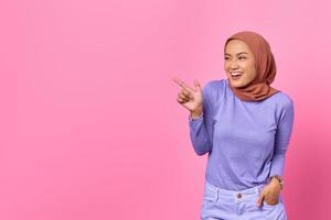 retrato, de, sonriente, joven, mujer asiática, señalar con el dedo, en, espacio de la copia, en, fondo rosa