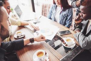 empresario de pueblo multiétnico, concepto de pequeña empresa. Mujer mostrando algo a sus compañeros de trabajo en la computadora portátil mientras se reúnen alrededor de una mesa de conferencias foto