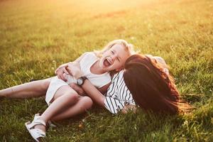 Mother plays with her daughter on the street in the park at sunset photo