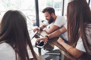 A group of young people with gadgets and a laptop arrange a brainstorm and communicate with each other. The concept of developing a young business photo