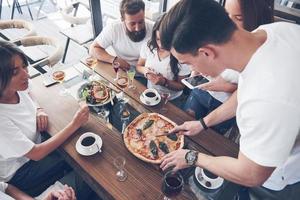 Sabrosa pizza en la mesa, con un grupo de jóvenes sonrientes descansando en el pub foto