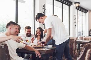 Tasty pizza on the table, with a group of young smiling people resting in the pub photo