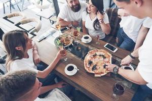 Sabrosa pizza en la mesa, con un grupo de jóvenes sonrientes descansando en el pub foto