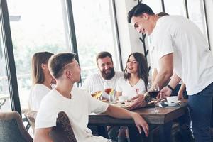 Sabrosa pizza en la mesa, con un grupo de jóvenes sonrientes descansando en el pub foto