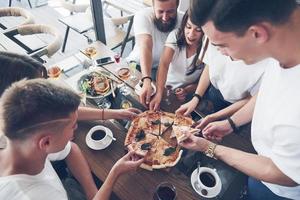 Sabrosa pizza en la mesa, con un grupo de jóvenes sonrientes descansando en el pub foto