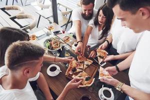 Sabrosa pizza en la mesa, con un grupo de jóvenes sonrientes descansando en el pub foto