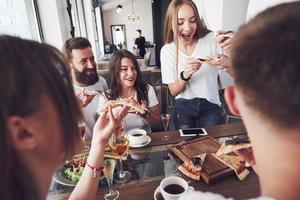 Sabrosa pizza en la mesa, con un grupo de jóvenes sonrientes descansando en el pub foto