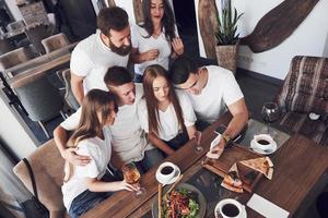 un grupo de personas hace una foto selfie en un café. los mejores amigos se reunieron en una mesa para cenar comiendo pizza y cantando varias bebidas