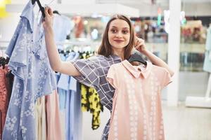 This dress is perfect. Young beautiful smiling woman makes choice when shopping at a store