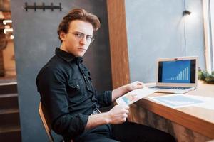 Businessman using laptop with tablet and pen on wooden table in coffee shop with a cup of coffee. An entrepreneur who manages his company remotely as a freelancer. photo